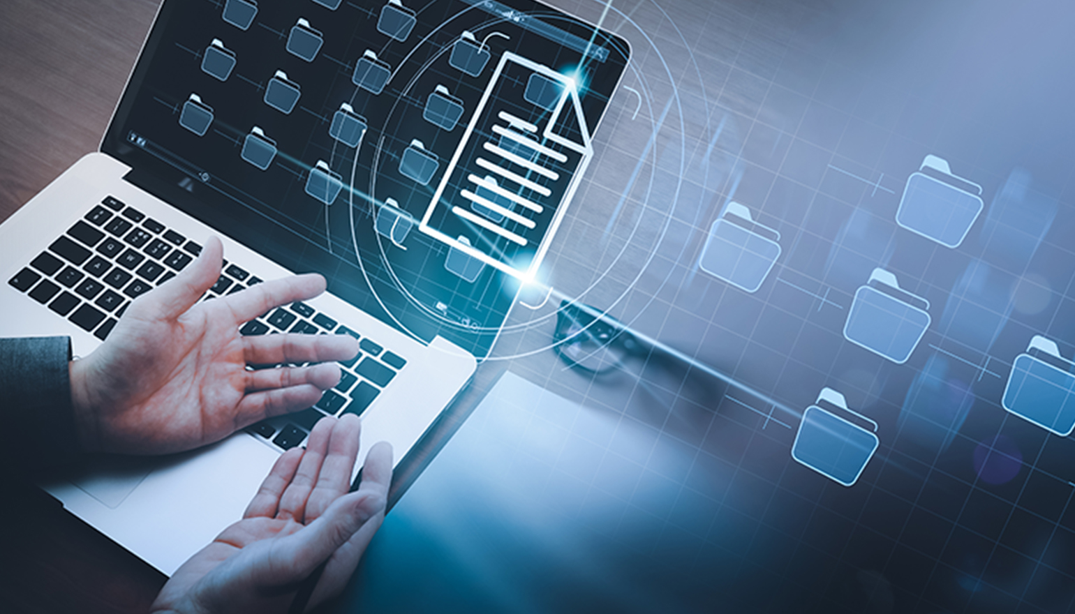 A man sitting at a desk holds his hands out with folder icons merging into one folder displayed on his laptop screen.
